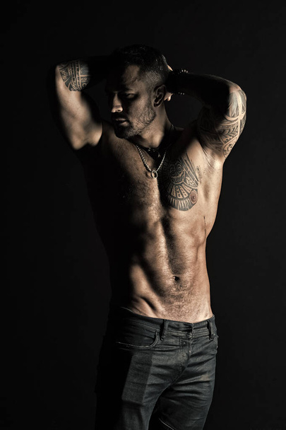 Sportsman with six pack and ab. Tattooed man show sexy muscular torso. Bodybuilder with biceps and triceps. Fashion model with tattoo in jeans. Bodycare with fitness and sport in vintage filter - Foto, imagen