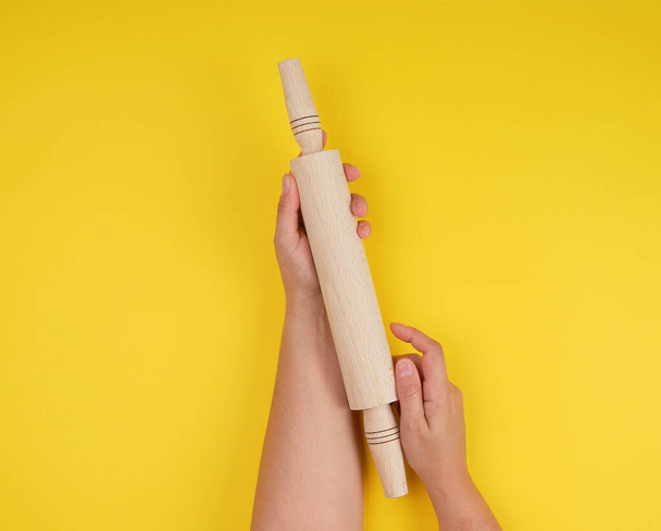 hand holding a wooden rolling pin on a yellow background - Photo, Image
