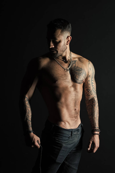 Bodycare with fitness and sport. Man with tattooed arm and chest. Bearded man with strong torso. Tattoo model with sexy belly. Sportsman or athlete in fashion jeans - Fotografie, Obrázek