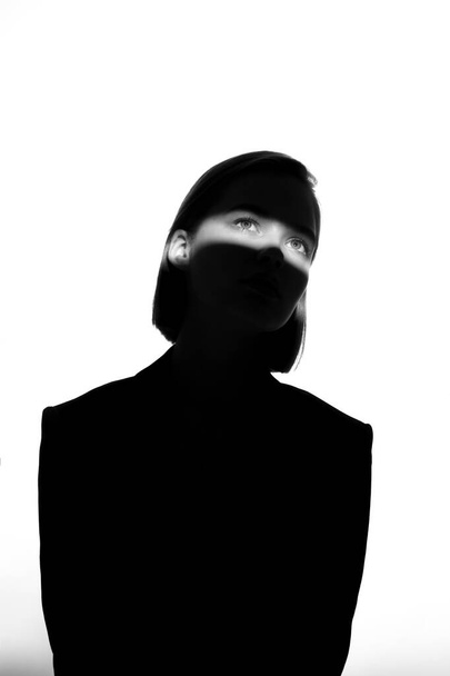 Fashionable beauty portrait. Black silhouette on white background. Girl with a spot of light on her face.  - 写真・画像