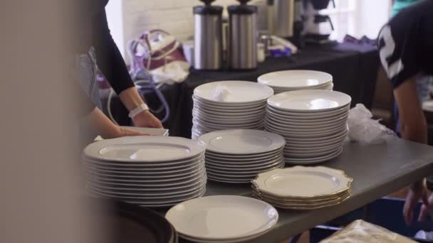 Vista de varios pares de manos poner racimo de platos blancos en la mesa oscura
 - Imágenes, Vídeo