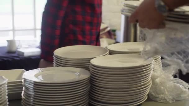 Několik párů rukou vybalit a dát hromadu bílých talířů na tmavý stůl - Záběry, video