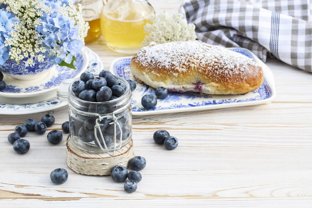 Jar with blueberries and fresh bun on white wooden table - Photo, image