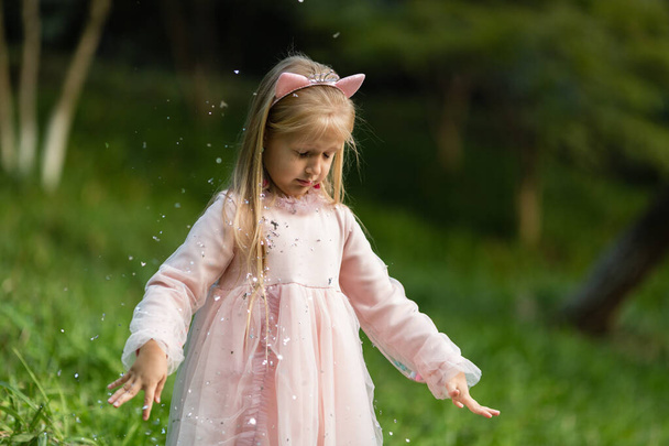 Niña con estilo con el pelo rubio lanzando confeti en el parque. Cumpleaños celebración al aire libre, diversión niño ocio
 - Foto, imagen