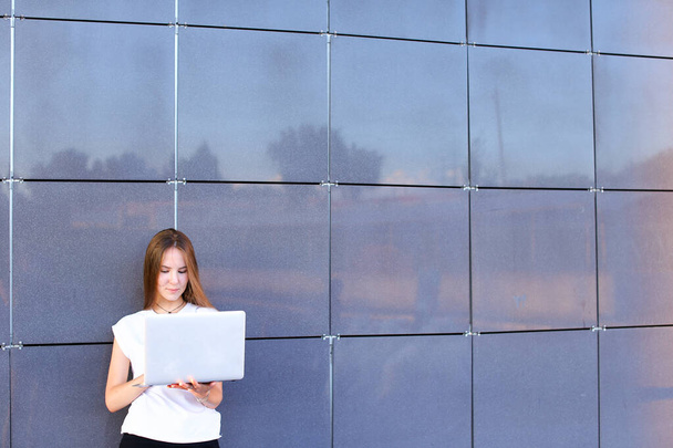 schöne junge Unternehmerin hält Laptop und arbeitet, löst Probleme und steht auf der Hintergrundwand des Business Centers. - Foto, Bild