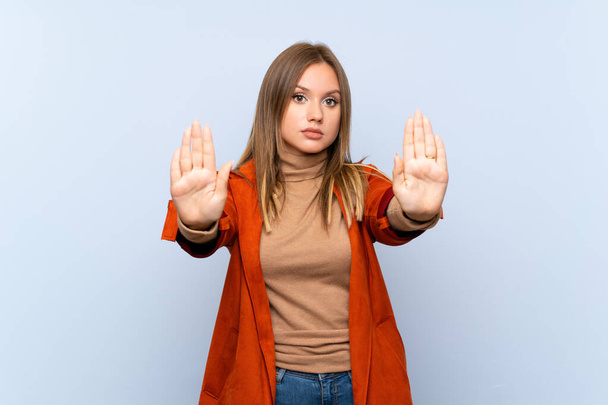 Teenager girl with coat over isolated blue background making stop gesture and disappointed - Fotografie, Obrázek