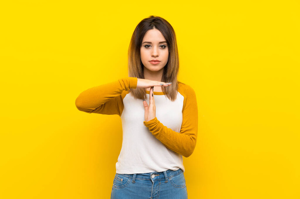 Mooie jonge vrouw over geïsoleerde gele muur maakt tijd uit gebaar - Foto, afbeelding