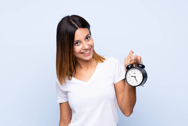Young woman over isolated blue background holding vintage alarm clock - Fotó, kép