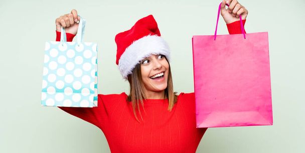 Mädchen mit Weihnachtsmütze und mit Einkaufstasche vor isoliertem grünen Hintergrund - Foto, Bild