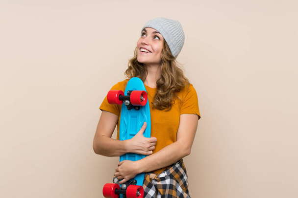Joven patinadora rubia sobre fondo aislado mirando hacia arriba mientras sonríe
 - Foto, Imagen