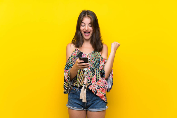 Cep telefonu kullanarak izole sarı arka plan üzerinde renkli elbiseli Kafkas kız - Fotoğraf, Görsel