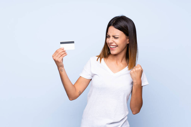 Soyutlanmış mavi arka planı olan genç bir kadın kredi kartı tutuyor. - Fotoğraf, Görsel