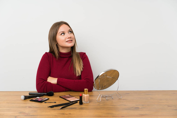 Chica adolescente con paleta de maquillaje y cosméticos en una mesa riendo
 - Foto, Imagen