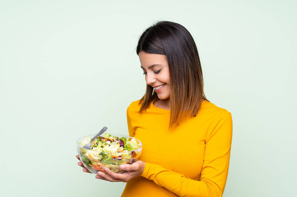 Young woman with salad over isolated green wall - Photo, Image