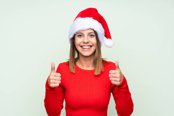 Girl with christmas hat over isolated green background giving a thumbs up gesture - Фото, изображение