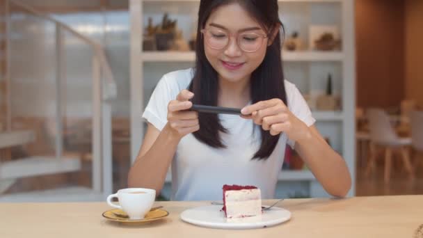 Bloggaaja Aasian ystävällinen naiset vaikuttaja syödä kakkua yöllä kahvilassa. Kaunis nuori nainen onnellinen rentoutua hauskaa teknologian avulla matkapuhelin ottaa kuvan hänen ruoka ladata sosiaalisessa mediassa yliopistolla kampuksella
. - Materiaali, video