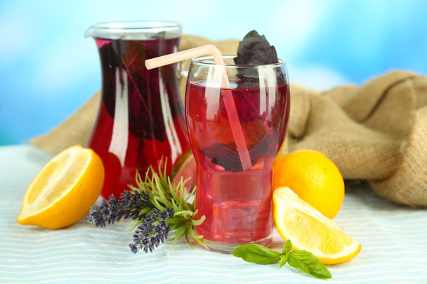 Red basil lemonade in jug and glass, on wooden table, on bright background - Foto, immagini