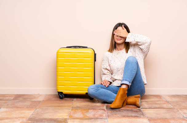 Мандрівник жінка з валізою сидить на підлозі, покриваючи очі руками
 - Фото, зображення