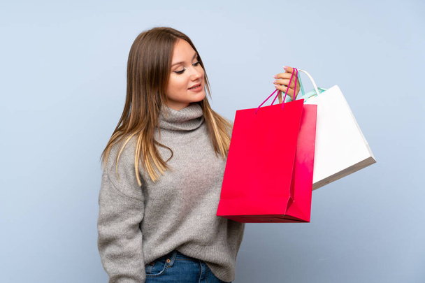 Teenager girl with sweater over isolated blue background holding a lot of shopping bags - Foto, afbeelding