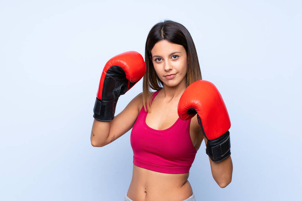Young sport woman over isolated blue background with boxing gloves - 写真・画像