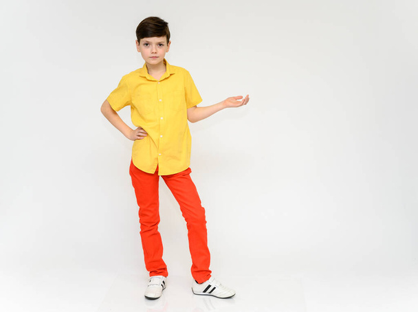 Teenager Schoolboy Boy Concept Shows Emotion. Full-length photo of a child in red pants and a yellow shirt on a white background in studio. Stands in front of the camera in various poses. - Foto, afbeelding