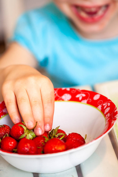 Close up of little girl taking from strawberry bowl - Фото, изображение