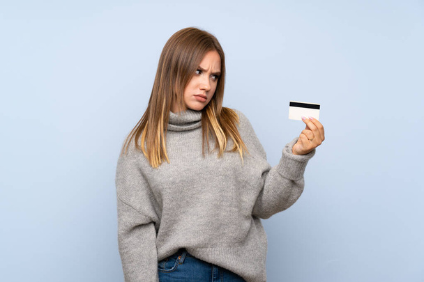 Bir kredi kartı tutan izole mavi arka plan üzerinde kazak ile Genç kız - Fotoğraf, Görsel
