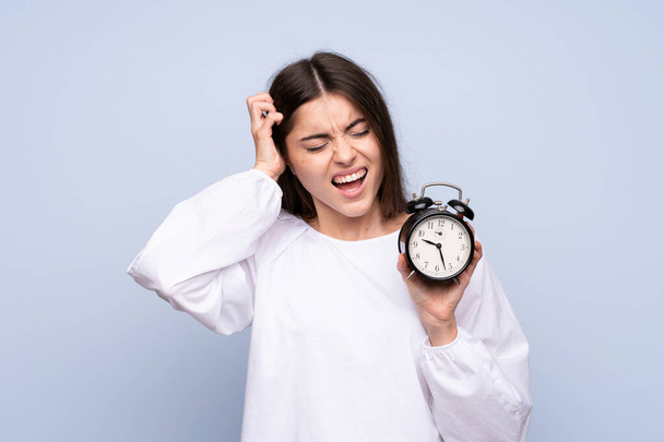 Young woman over isolated blue background holding vintage alarm clock - Fotó, kép