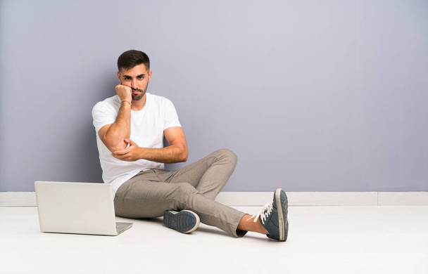 Молодий чоловік зі своїм ноутбуком сидить на одній підлозі незадоволений і розчарований
 - Фото, зображення