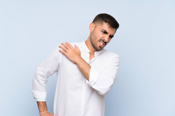 Pohledný muž s plnovousem přes izolované modré pozadí trpí bolestí v rameni za to, že vynaložil úsilí - Fotografie, Obrázek