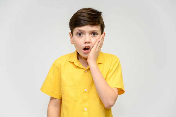 Concept boy teenager shows imitates the behavior of heroes from different movies. Portrait of a child on a white background in a yellow shirt. Standing in front of the camera in poses with emotions. - Photo, Image