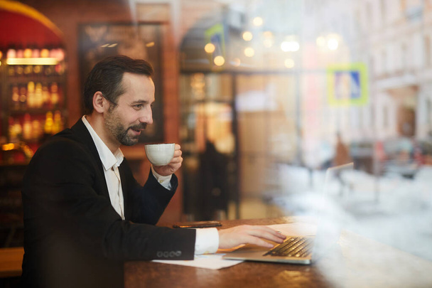 Vista lateral retrato de homem de negócios maduro sorrindo apreciando xícara de café sentado à mesa no café, espaço de cópia
 - Foto, Imagem