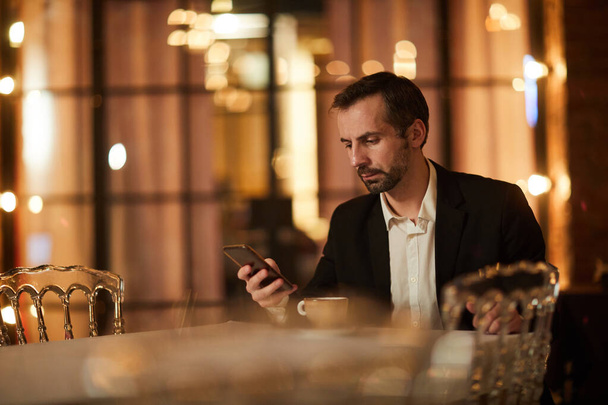 Portré jóképű érett úriember ellenőrzi a telefonüzeneteket, miközben várja a dátumot az étteremben, másolás helyet - Fotó, kép