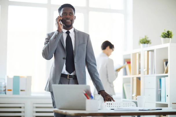 Retrato de un hombre de negocios afroamericano sonriente hablando por teléfono mientras está parado en el lugar de trabajo en la oficina, espacio para copiar
 - Foto, imagen