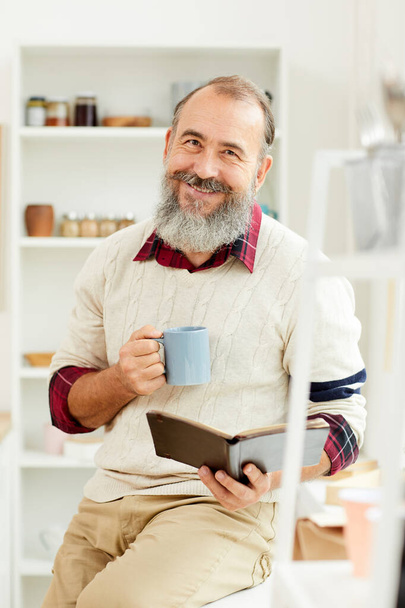 朝コーヒーを飲みながら本を読みながらカメラで元気に微笑む髭の先輩の肖像 - 写真・画像
