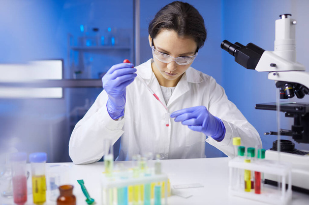 Portrait of young female scientist preparing blood sample using dropper while working on medical research in laboratory, copy space - Photo, Image