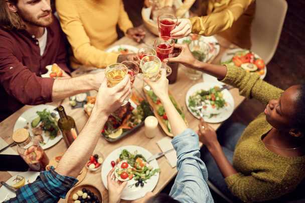 Powyżej widoku ludzi podnoszących szklanki nad stołem przy kolacji, ciesząc się imprezą z przyjaciółmi, przestrzeń kopiowania - Zdjęcie, obraz