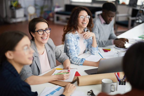 Portret wielobranżowego zespołu biznesowego uśmiechającego się radośnie, dyskutującego o kreatywnym projekcie podczas spotkania w biurze - Zdjęcie, obraz