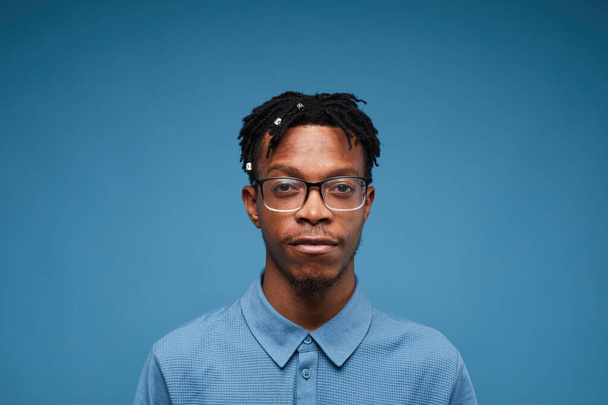 Портрет головы и плеч молодого афроамериканца, смотрящего в камеру, позирующего на синем фоне, копирующего пространство
 - Фото, изображение