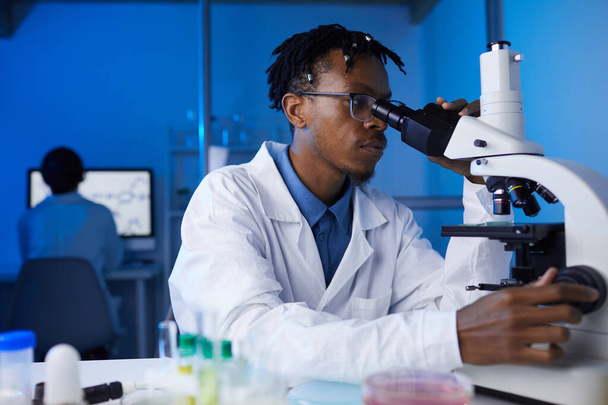 研究室で医学研究をしながら顕微鏡を見ているアフリカ系アメリカ人青年の肖像画、コピースペース - 写真・画像