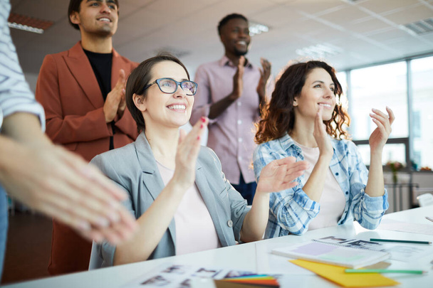 Low angle portrait of creative team clapping happily while celebrating success in office, focus on two smiling young women in foreground - Fotografie, Obrázek