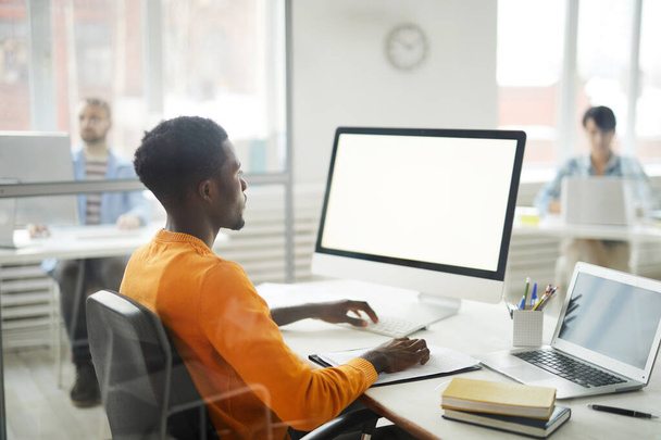 Widok z boku portret młodego Afroamerykanina korzystającego z komputera w biurze, skupienie się na białym ekranie, przestrzeń do kopiowania - Zdjęcie, obraz