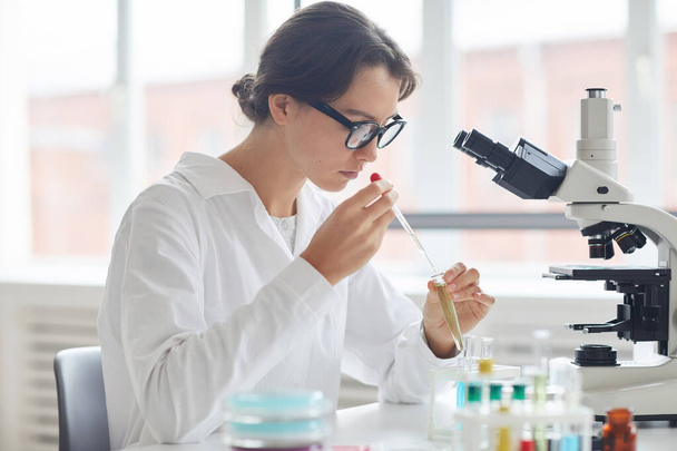 Portrait latéral d'une belle jeune femme travaillant en laboratoire, préparant des échantillons d'essai pour la recherche au microscope
 - Photo, image