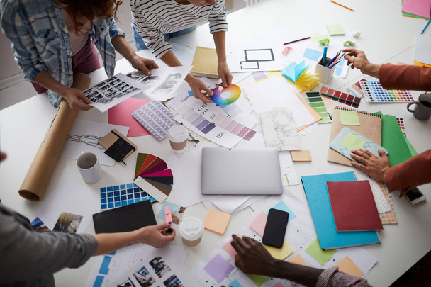 Primer plano de alto ángulo del equipo creativo de negocios que trabaja en el proyecto de diseño se centran en la mesa con fotografías y muestras de color dispersas, espacio de copia
 - Foto, imagen