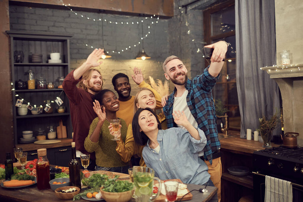 Çok ırklı bir grup genç, parti ve akşam yemeğinin tadını çıkarırken akıllı telefondan selfie çekiyor. - Fotoğraf, Görsel