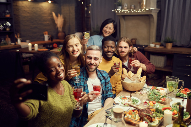 Grupo multiétnico de jóvenes que toman fotos selfie a través de un teléfono inteligente mientras disfrutan de una cena en casa, espacio para copiar
 - Foto, Imagen