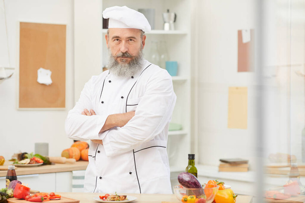 Cintura até retrato de barbudo chef sênior posando com confiança enquanto está de pé na cozinha do restaurante, espaço de cópia
 - Foto, Imagem
