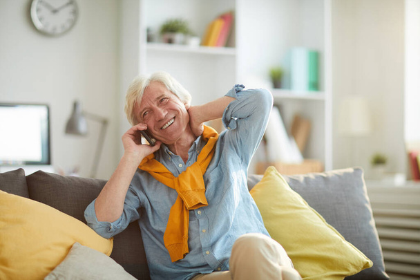 Portrait of smiling senior man speaking by smartphone while relaxing sitting on comfortable couch at home, copy space - Photo, Image