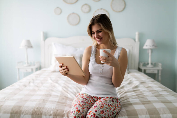 mooie jonge vrouw met behulp van digitale tablet in bed - Foto, afbeelding