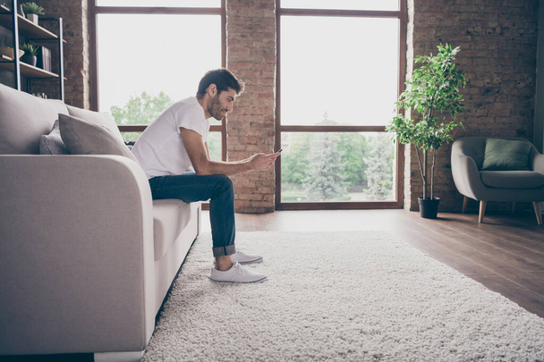Profile photo of mixed race guy sitting cozy sofa holding telephone reading positive news texting with girlfriend love letters wear casual outfit flat loft living room indoors - Foto, Imagen